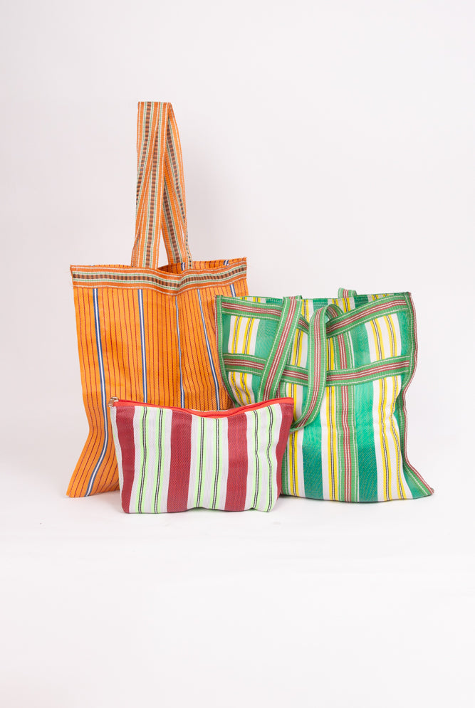 The three bags included in the Grab and Go Market Set sit together. Two of the bags are identical in size, and are large, square totes with shoulder straps. The third bag is a smaller zipper pouch that is wider than it is tall. All three bags are made of upcycled nylon with a stripe pattern, but the colors vary on each.