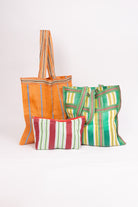 The three bags included in the Grab and Go Market Set sit together. Two of the bags are identical in size, and are large, square totes with shoulder straps. The third bag is a smaller zipper pouch that is wider than it is tall. All three bags are made of upcycled nylon with a stripe pattern, but the colors vary on each.