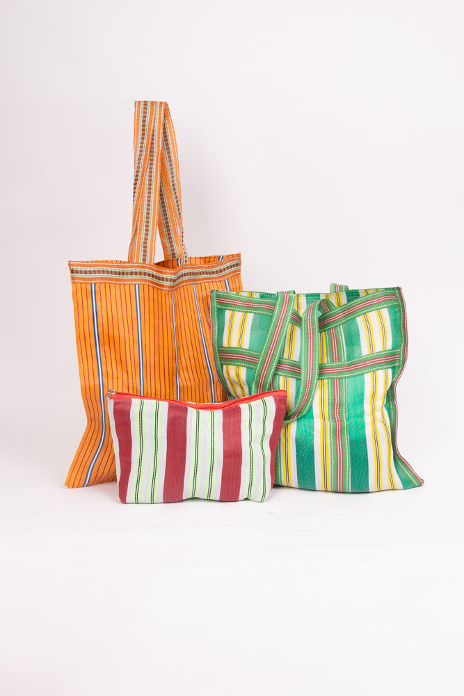 The three bags included in the Grab and Go Market Set sit together. Two of the bags are identical in size, and are large, square totes with shoulder straps. The third bag is a smaller zipper pouch that is wider than it is tall. All three bags are made of upcycled nylon with a stripe pattern, but the colors vary on each.