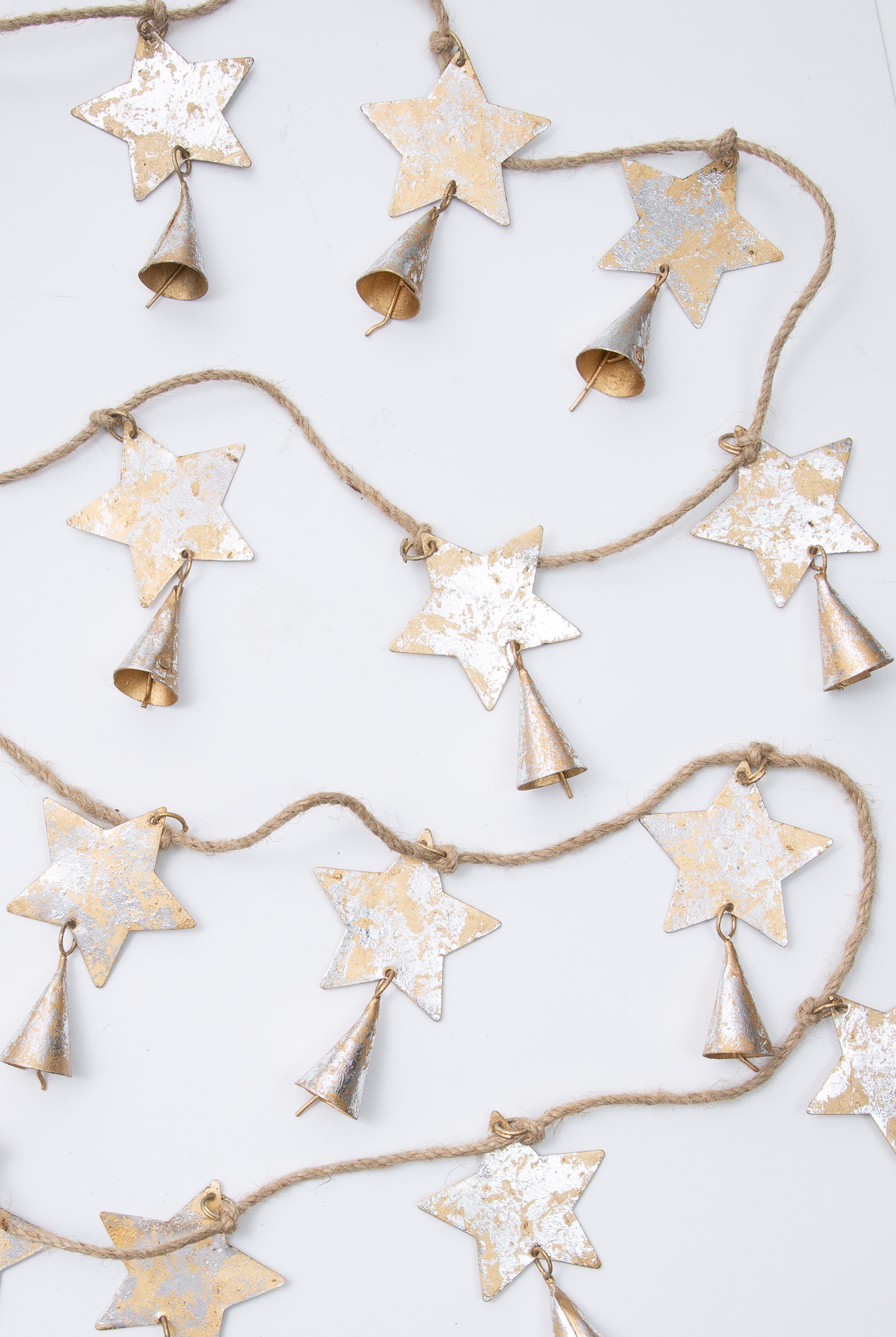 This is a rustic style rope garland with flat, metallic stars attached at regular intervals. The stars are silver and gold metal with a weathered look. There is a metallic cone-shaped bell attached to each star.