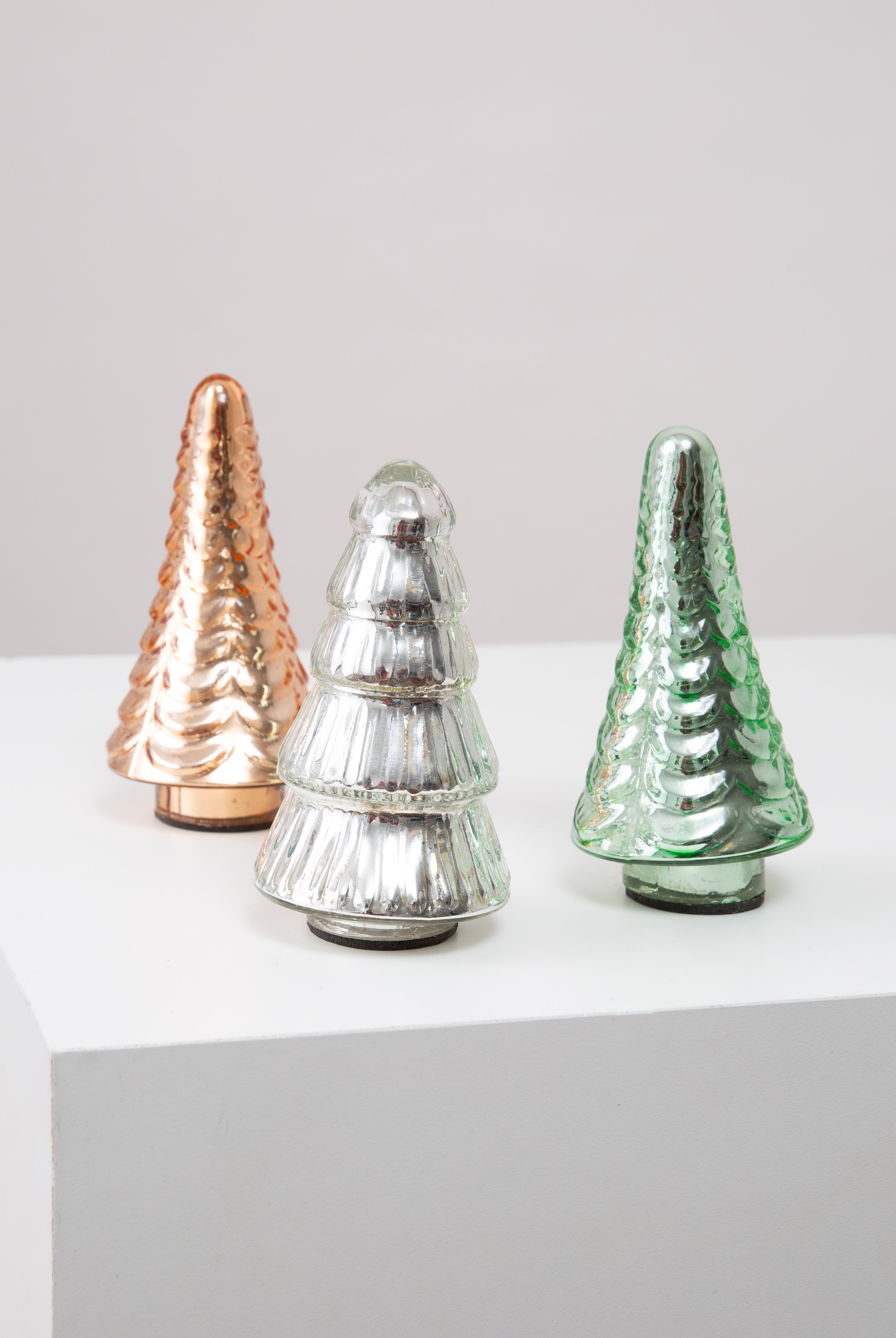 The three trees included in the Glass Tree Set are shown. They are roughly the same size, but each is composed of a different colored glass. One is amber, one silver, and one green. Two of the trees have the same textured pattern, and one has a different pattern that makes it look like it has cascading layers of branches.