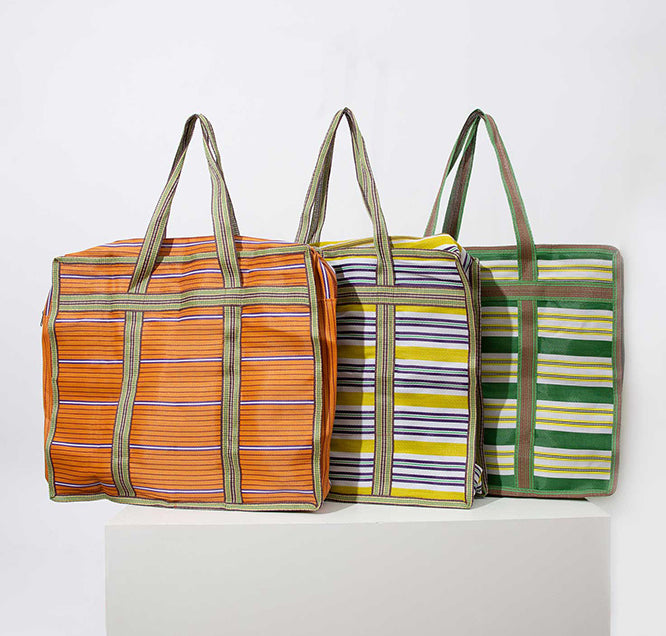 Three of the XL Market Totes are shown grouped together. Each is made of upcycled nylon fabric with a stripe pattern, but each is a different color. One is green and orange, one is blue and yellow, and one is green and yellow.