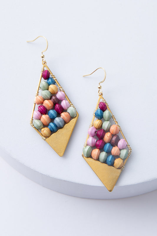 The Abacus Earrings are dangly earrings with a diamond shape. The outline of the earrings is brass wire. Multiple rows of rainbow colored paper beads are strung inside the diamond, and at the bottom of the earrings there is a triangle made of solid brass.