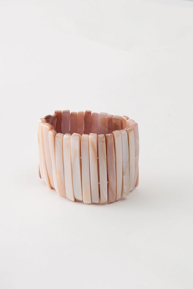 The Beachcomber Bracelet is composed of many tall strips of shell strung along elastic. The shell pieces vary in color, but each has peach and white tones.