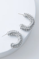 These are silver demi-hoop earrings that are open at the back. They are composed of silver thread and silver beads crocheted together to form a chunky hoop.