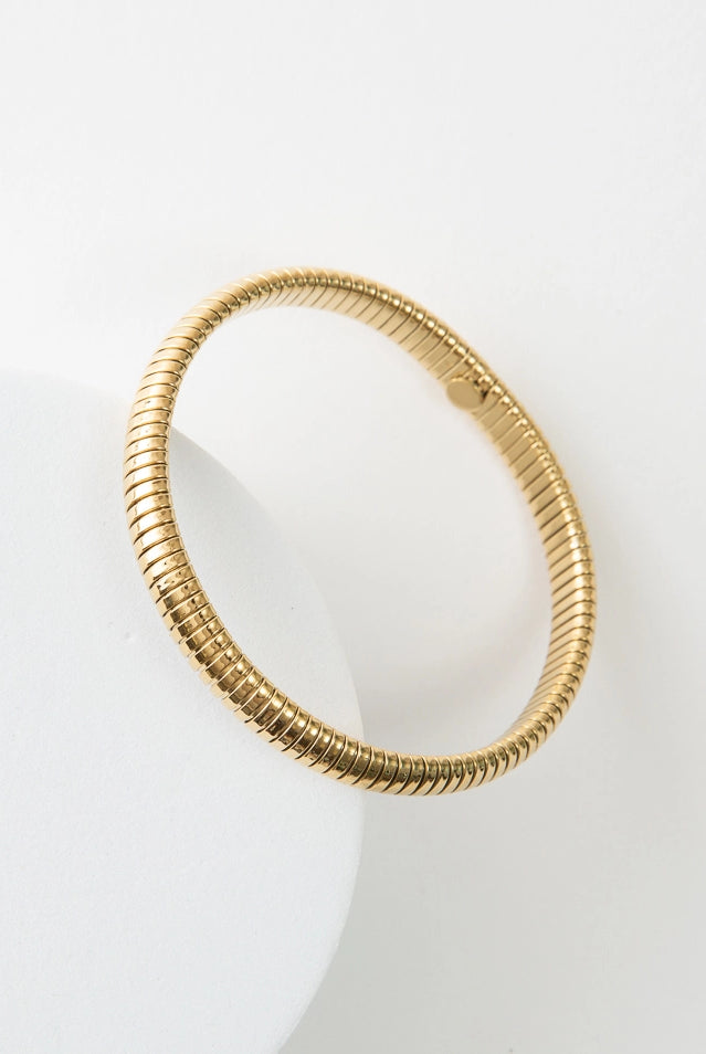 The Cobra Bracelet is a thin, simple gold bracelet. It has a banded texture that gives the look of a coil of shining gold wrapping around the wrist.