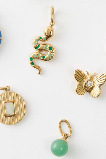 A collection of gold-plated charms in various designs, including shapes of a moon, heart, and butterfly, displayed against a white background.