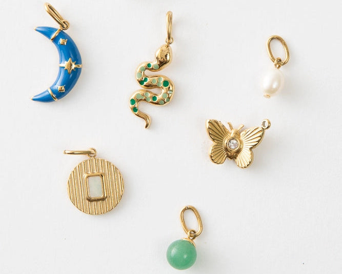 A collection of gold-plated charms in various designs, including shapes of a moon, heart, and butterfly, displayed against a white background.