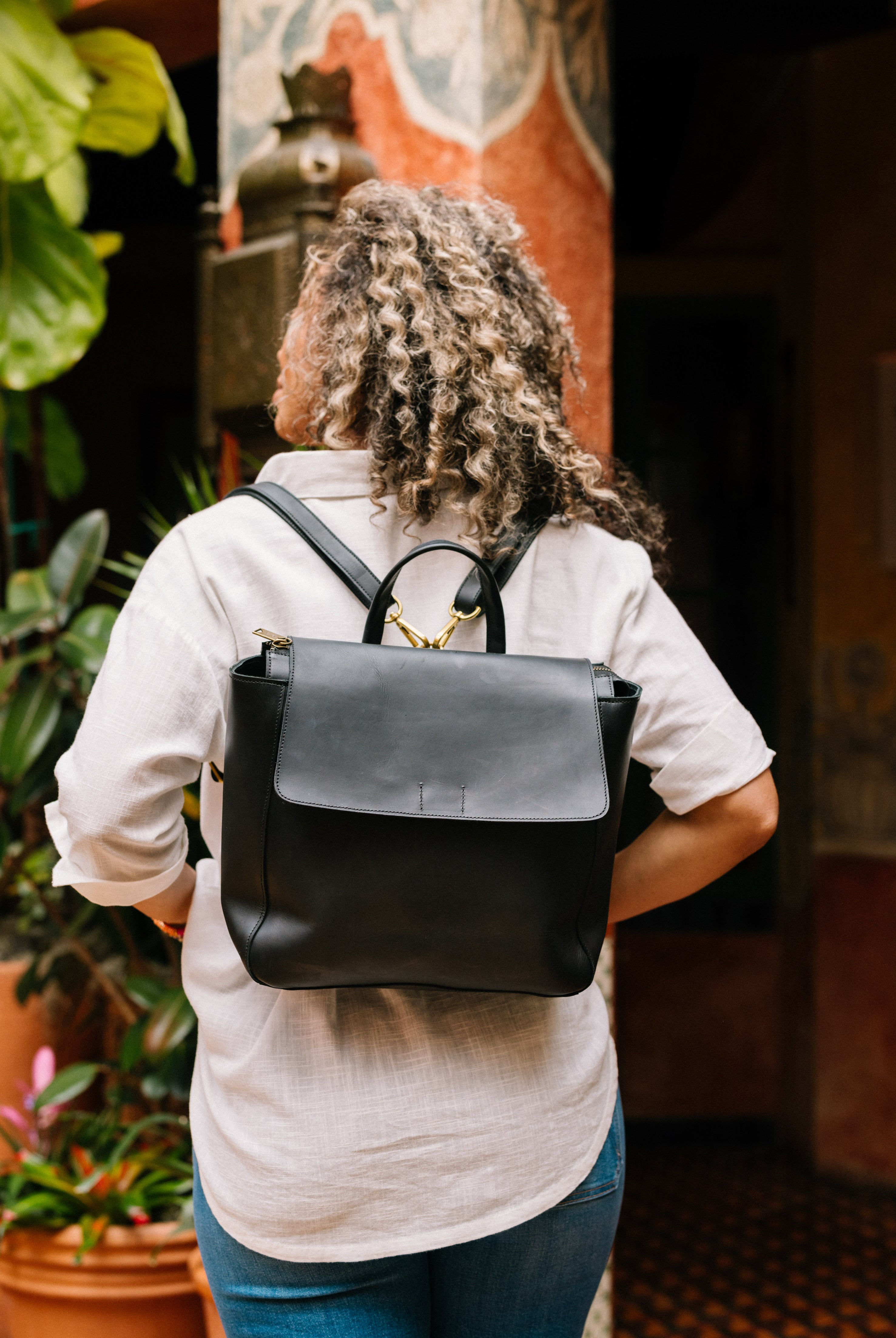 The interior back wall of the Debut Backpack is shown. The bag has a pink fabric lining with a white floral print. There is an interior zipper pocket stitched into the back wall. There is also a larger slot pocket along the back wall with a snap closure to keep it secure.