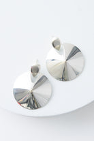 The Defender Earrings are circular disc earrings composed of shining silver. The silver discs are attached to silver ear posts. The discs slope up towards the middle, creating a raised center.