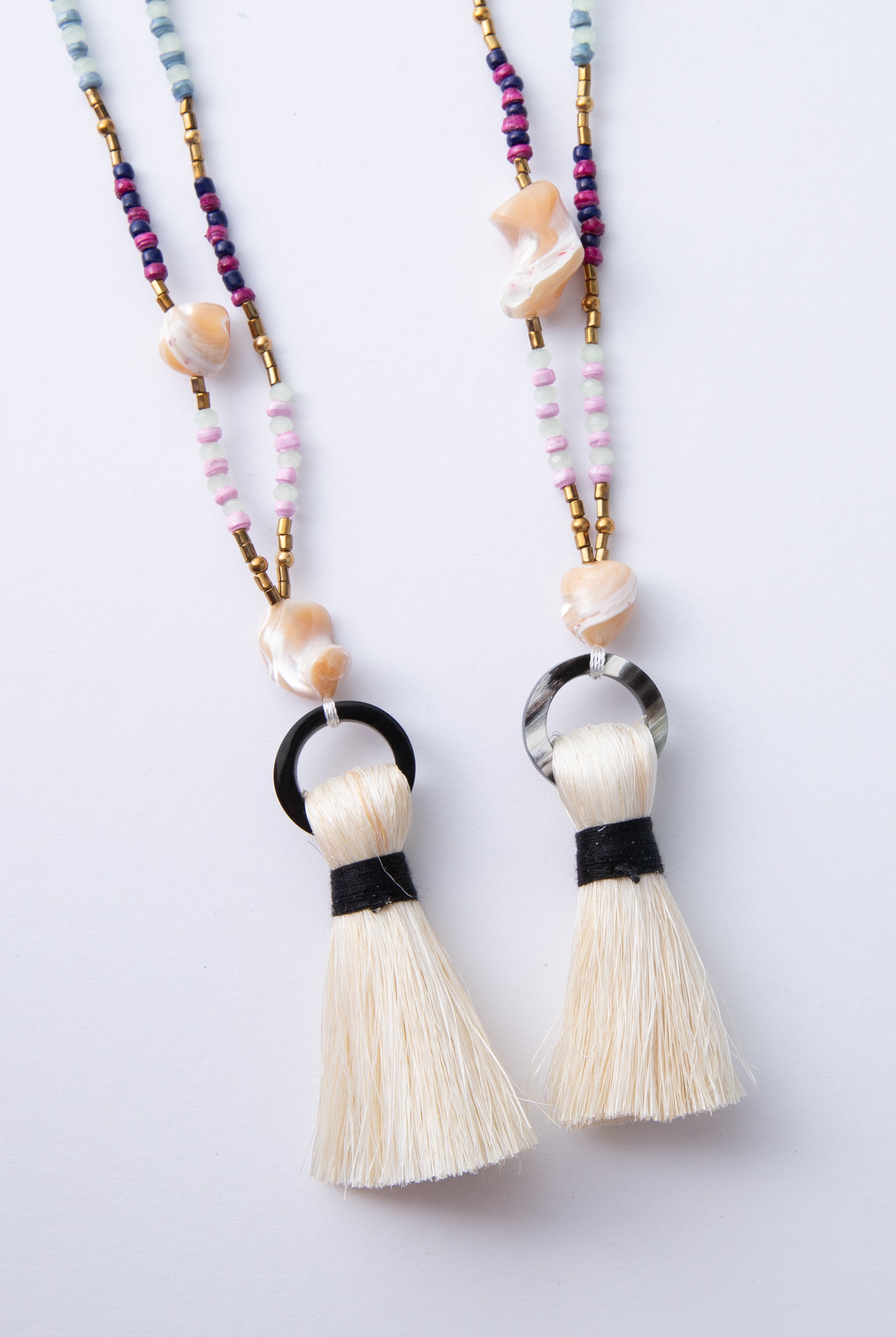 Two Dorah Necklaces are shown side by side. The horn circle at the bottom of each necklace varies in shade due to the natural material used to craft it. One is solid black, while the other is black with white streaks.