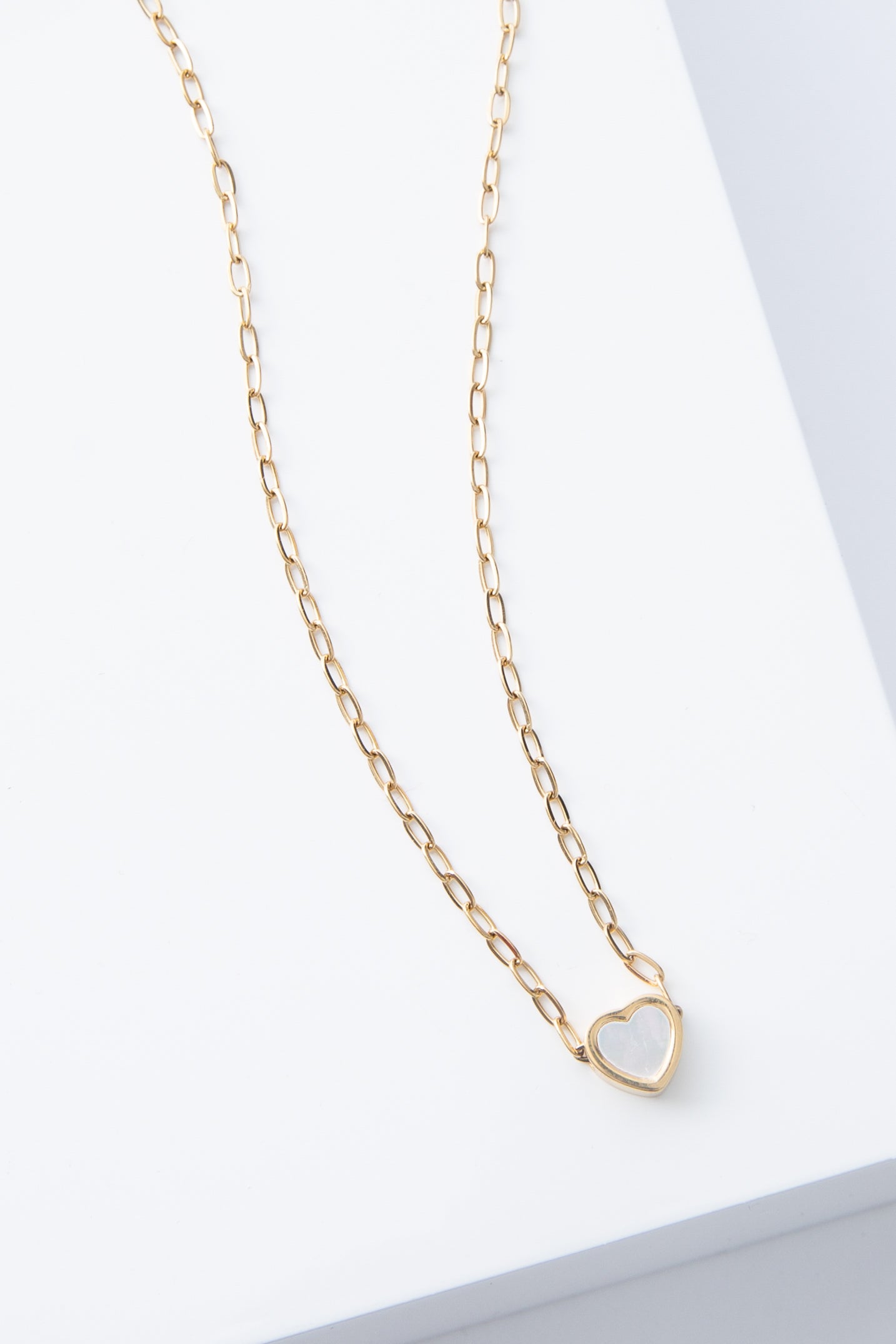 The Full Heart Necklace is a short, dainty necklace with a gold chain. At the bottom of the chain is a small heart pendant composed of shining mother-of-pearl and outlined in gold.