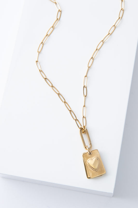 The Heart Keeper Necklace is a gold locket necklace with a gold chain composed of oval-shaped links. The locket pendant is suspended from a gold hoop. It is composed of two pieces of rectangular gold metal that can swing apart, allowing a photograph to be sandwiched between them. The piece on top has a raised heart design in the center.