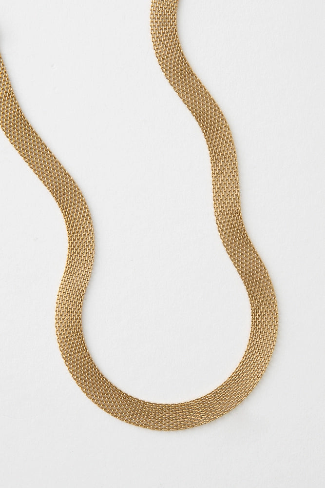 The Interwoven Necklace is a short, ribbon-style necklace composed entirely of gold plated metal links. The tiny links form a broad, flat chain.