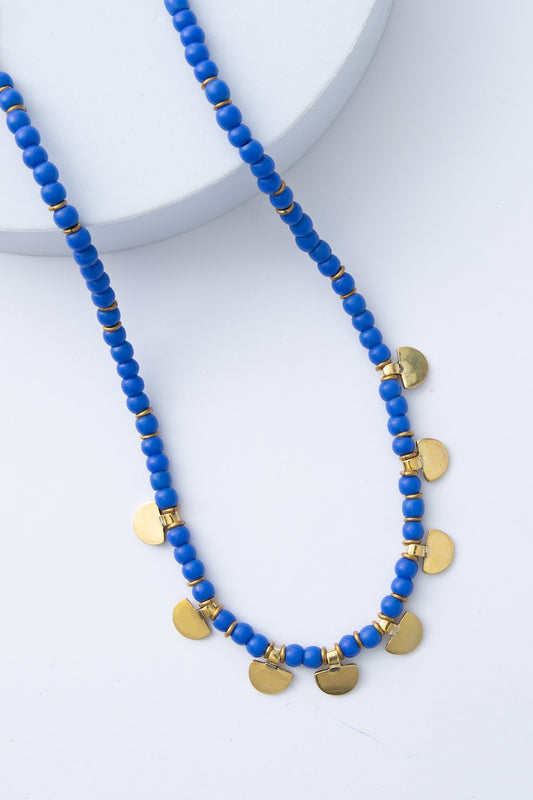 The Kobalti Necklace is composed of a single strand of bright blue glass beads accented by dainty brass rings. At the bottom of the necklace, semi-circles made of solid brass hang down between the blue beads at regular intervals.