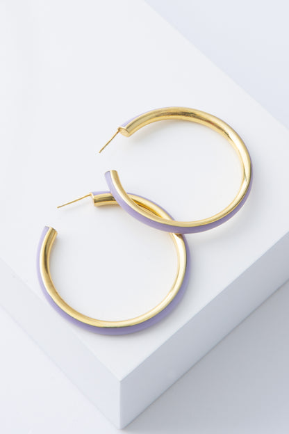 The Maddie Hoops are large hoop earrings. The interior rim of the hoop is gold plated bronze. The exterior rim is lavender colored resin. The two materials are fused together seamlessly. 