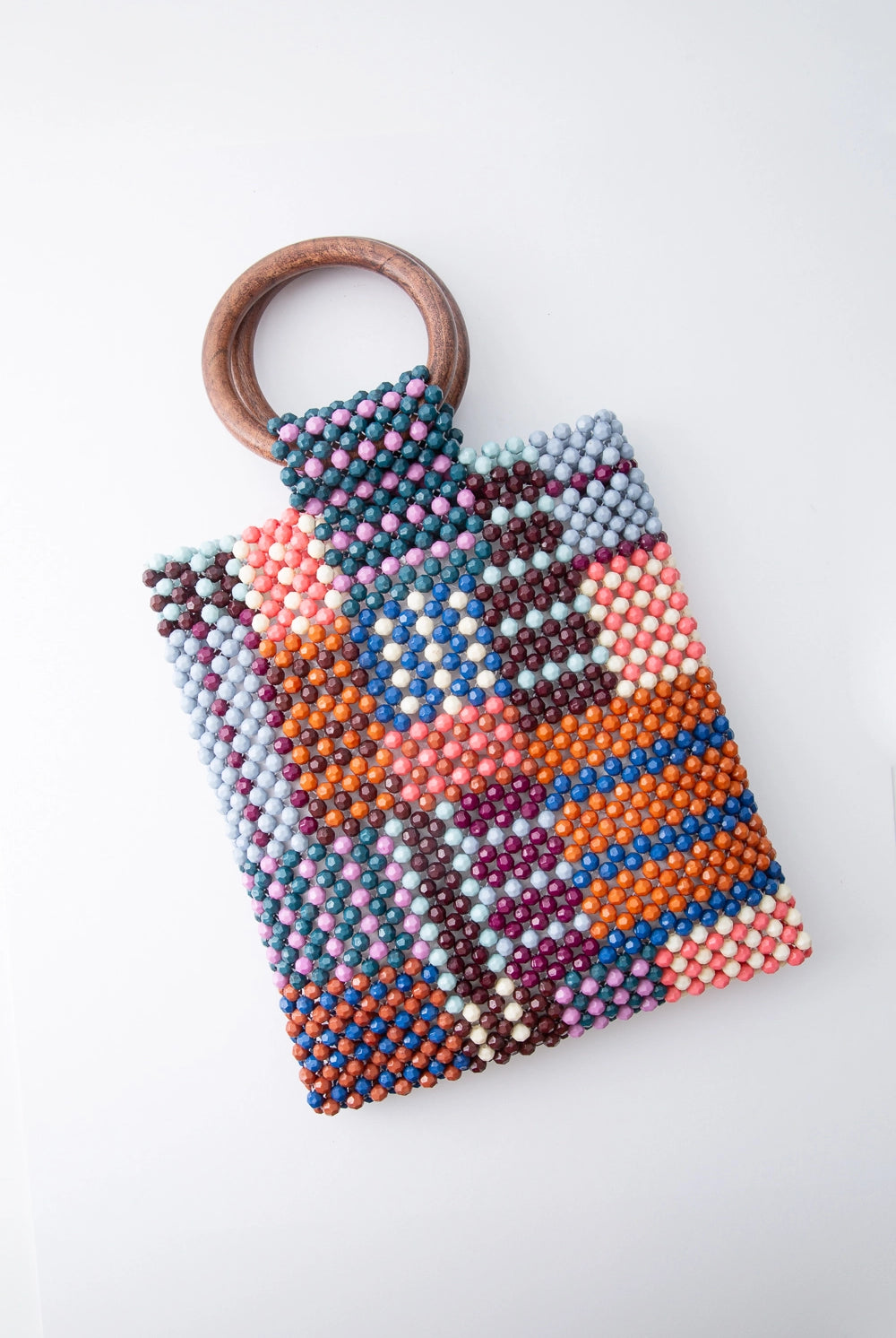 This small beaded bag is taller than it is wide. It is composed of many colored beads stitched into an irregular grid pattern, with alternating stripes and blocks of color. There are two round wooden handles attached to the top of the bag.
