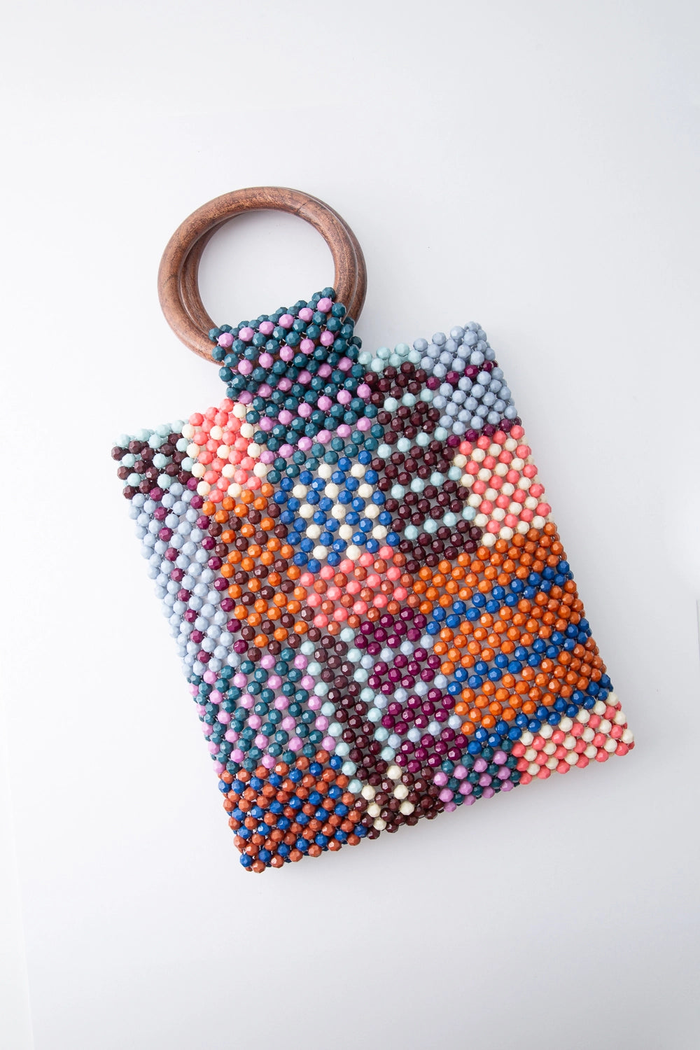 This small beaded bag is taller than it is wide. It is composed of many colored beads stitched into an irregular grid pattern, with alternating stripes and blocks of color. There are two round wooden handles attached to the top of the bag.