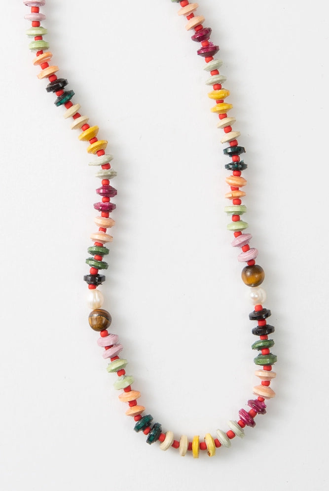 The Mihingo Necklace is a short beaded rope necklace. It is composed of many different colored disc-shaped paper beads. The beads are pink, mint, dark green, yellow, cream, and orange. The disc-shaped beads alternate with small red glass beads. Near the middle of the necklace there are accents of pearl and tiger's eye beads.