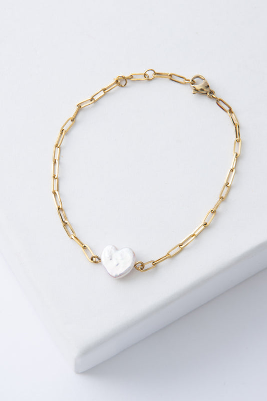The Opaline Bracelet is a gold chain link bracelet. At the center is a small, shining heart carved from freshwater pearl. The clasp can be adjusted to fit a variety of wrist sizes.