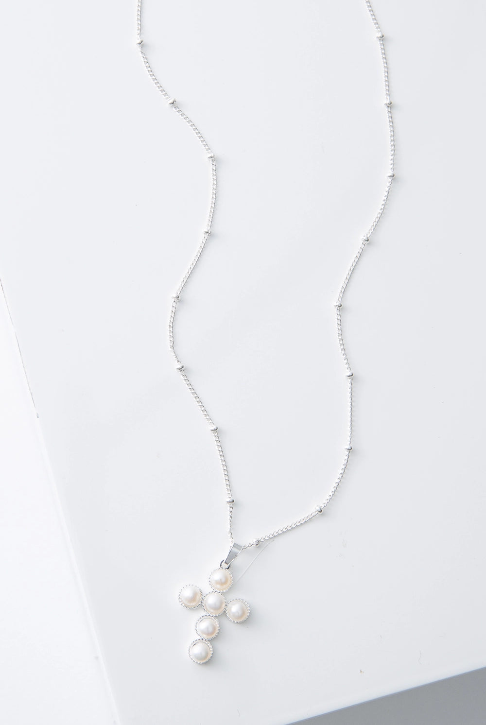 This is a dainty necklace with a silver chain studded with small, round silver beads every inch or so. The necklace has a small pendant composed of silver and six small round pearls arranged to form a cross shape.