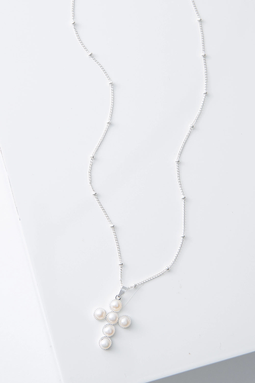 This is a dainty necklace with a silver chain studded with small, round silver beads every inch or so. The necklace has a small pendant composed of silver and six small round pearls arranged to form a cross shape.