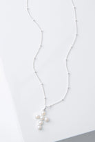 This is a dainty necklace with a silver chain studded with small, round silver beads every inch or so. The necklace has a small pendant composed of silver and six small round pearls arranged to form a cross shape.