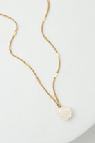 The Petite Bloom Necklace has a dainty gold chain with a small white flower pendant. The flower is composed of shining mother-of-pearl.