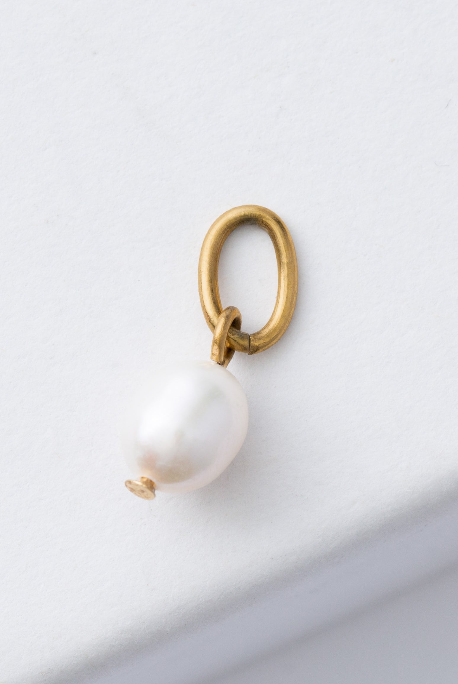 The Refine Charm is composed of a shining, oval-shaped pearl attached to a brass loop.