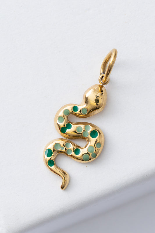 The Renew Charm features a winding gold snake charm attached to a brass loop. The snake is studded with light and dark green enamel dots along the length of its body.