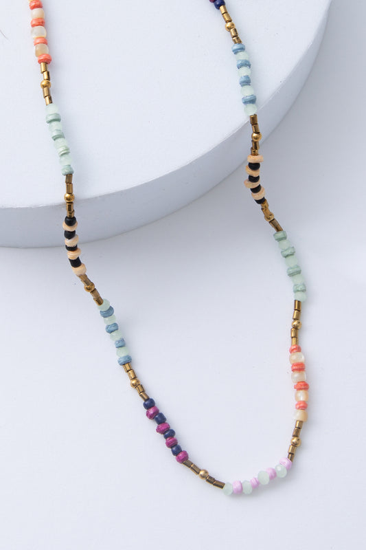 The Saltwater Necklace is a rope necklace composed of small paper beads in shades of mint, purple, and cream. The paper beads alternate with small brass beads and glass beads for a color-blocked look.