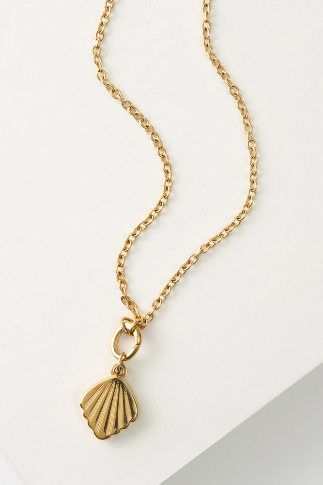 The Shell Cove Locket is a gold chain necklace with a gold shell-shaped locket. The shell has a minimalist, art deco-style design.