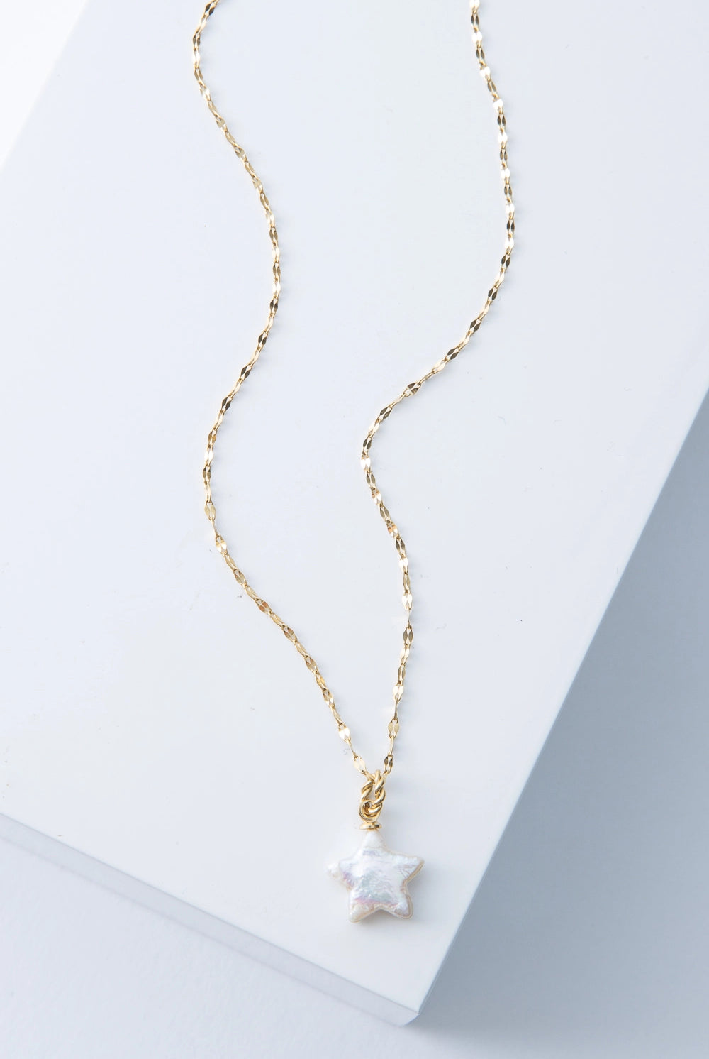 This necklace has a dainty gold chain with tiny flattened links. At the base of the chain is a small three-dimensional star charm composed of gleaming freshwater pearl.