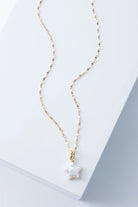 This necklace has a dainty gold chain with tiny flattened links. At the base of the chain is a small three-dimensional star charm composed of gleaming freshwater pearl.