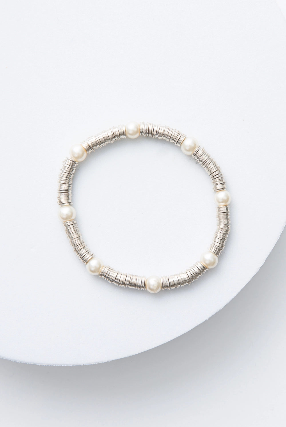 This is a single-strand bracelet composed of hundreds of sequin-like silver discs made of shining metal. Every inch or so, there is a round glass pearl strung between the metal sequins.