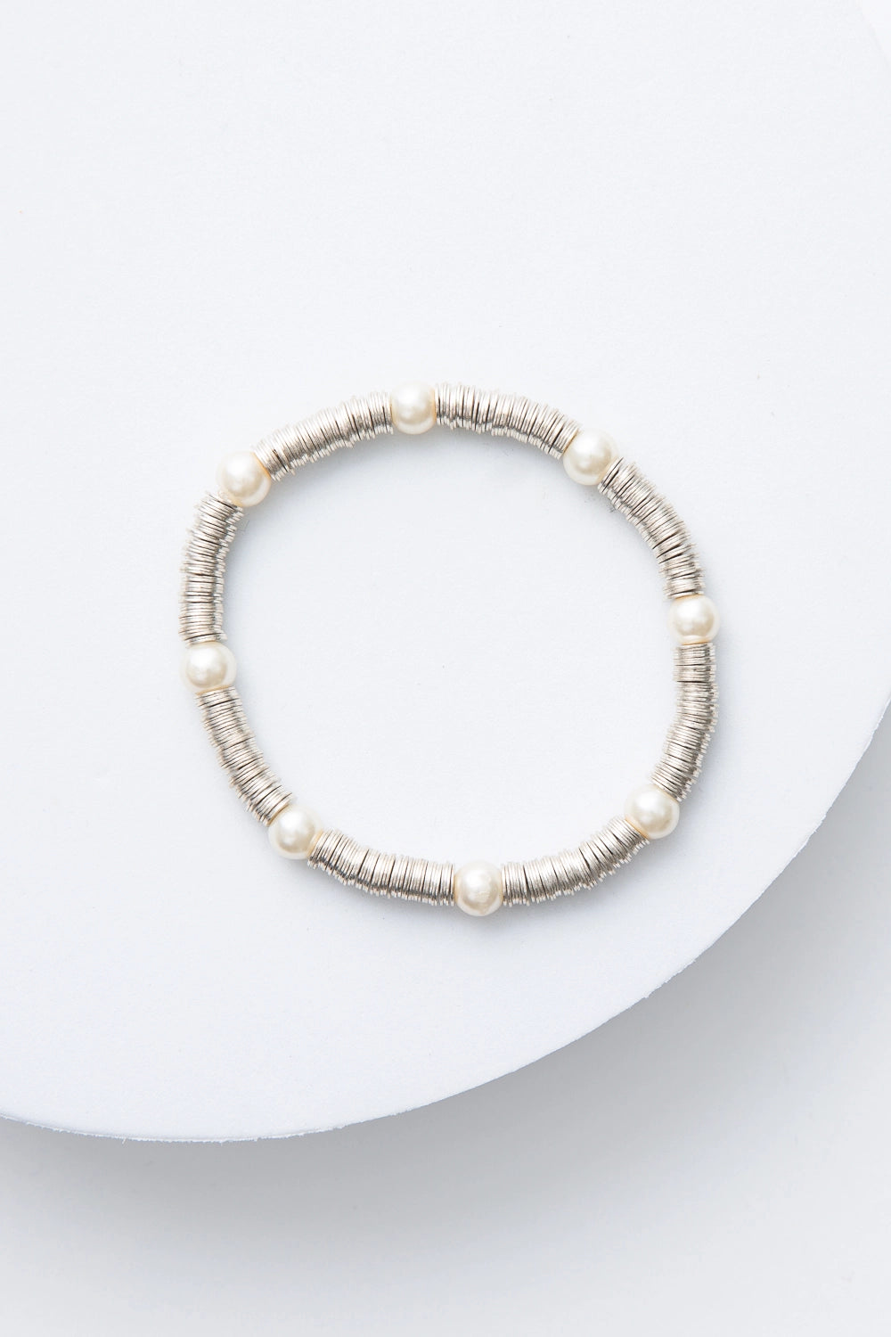 This is a single-strand bracelet composed of hundreds of sequin-like silver discs made of shining metal. Every inch or so, there is a round glass pearl strung between the metal sequins.