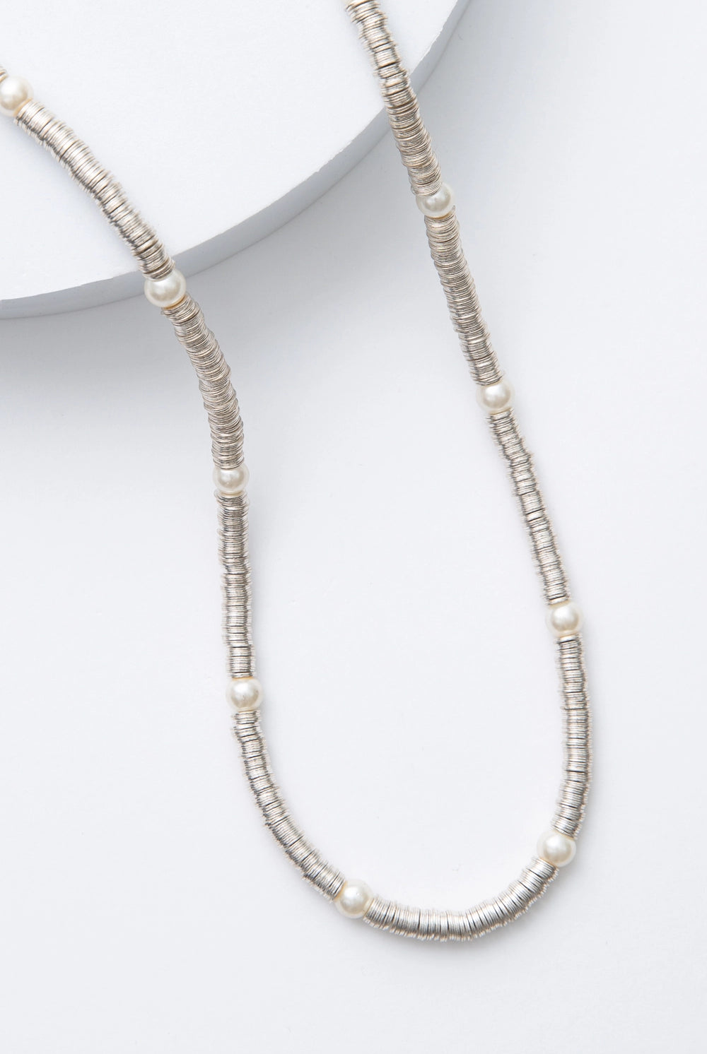 This is a single-strand necklace composed of hundreds of sequin-like silver discs made of shining metal. Every few inches, there is a round glass pearl strung between the metal sequins.