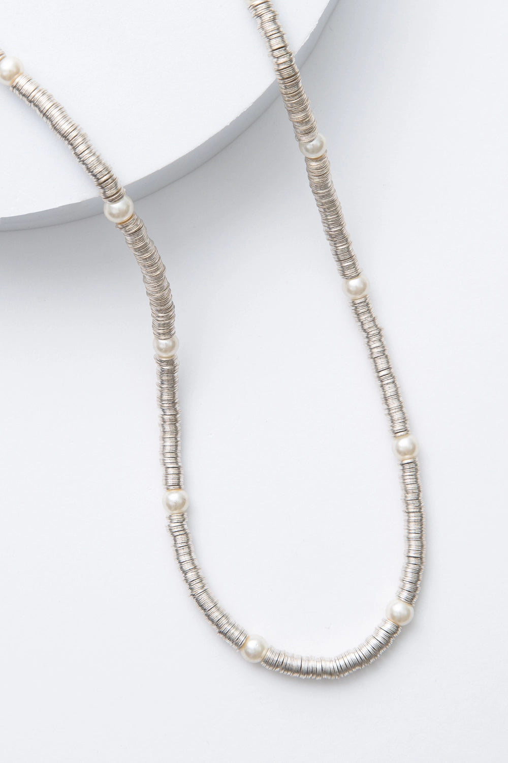 This is a single-strand necklace composed of hundreds of sequin-like silver discs made of shining metal. Every few inches, there is a round glass pearl strung between the metal sequins.