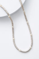 This is a single-strand necklace composed of hundreds of sequin-like silver discs made of shining metal. Every few inches, there is a round glass pearl strung between the metal sequins.