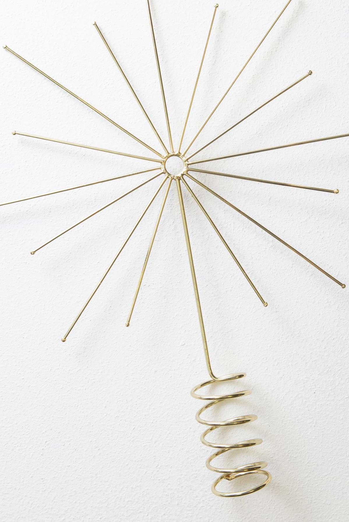 The Starburst Tree Topper is composed of shiny gold metal. It has a coiled base where the topper can be attached to the top of a tree. Above this, the metal forms a minimalist starburst design with a midcentury modern look.