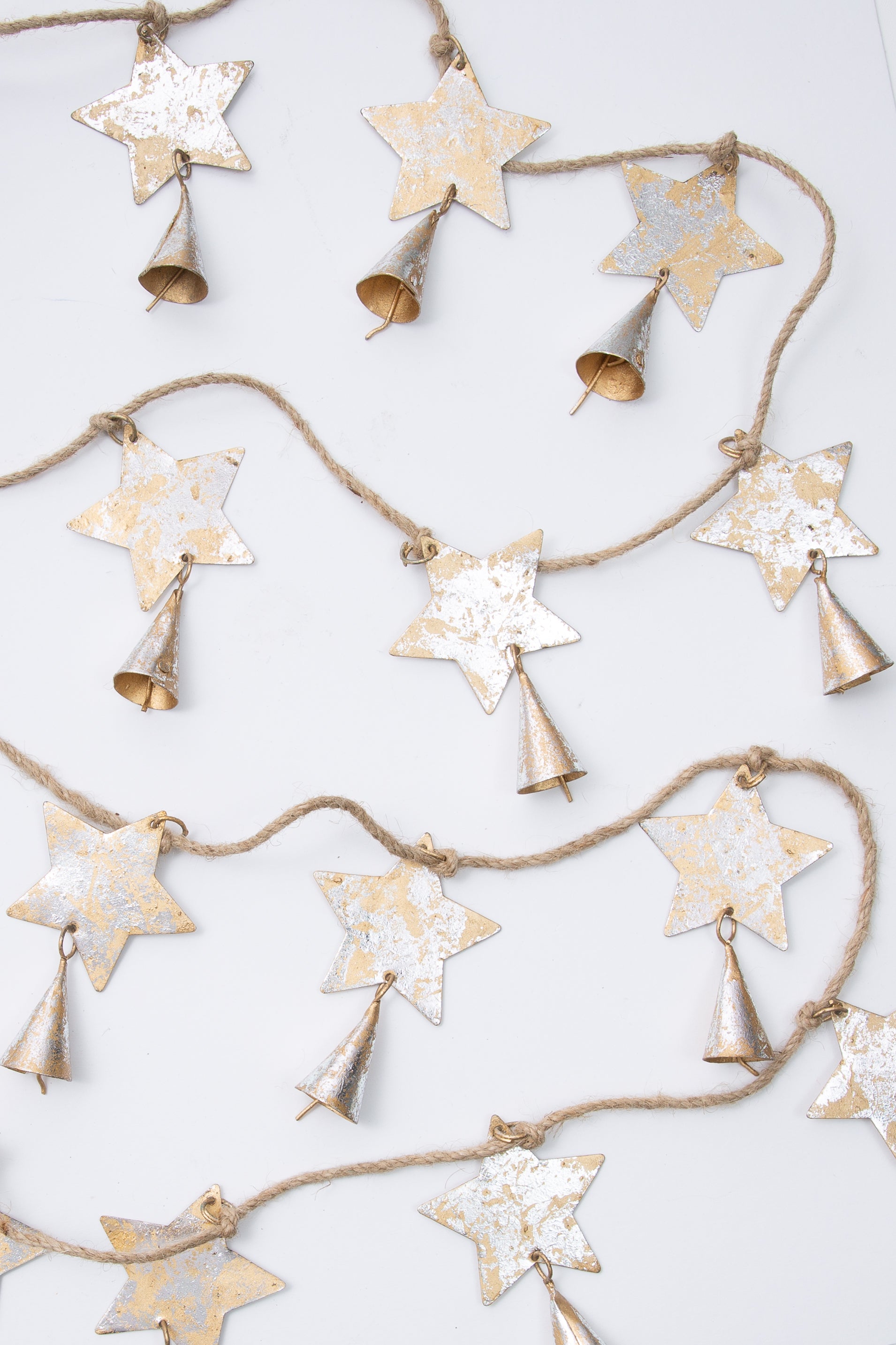 This is a rustic style rope garland with flat, metallic stars attached at regular intervals. The stars are silver and gold metal with a weathered look. There is a metallic cone-shaped bell attached to each star.