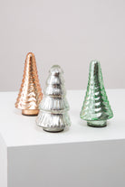 The three trees included in the Glass Tree Set are shown. They are roughly the same size, but each is composed of a different colored glass. One is amber, one silver, and one green. Two of the trees have the same textured pattern, and one has a different pattern that makes it look like it has cascading layers of branches.
