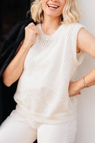 The Cloudburst Sweater Vest is worn over a white camisole. The sweater vest is white and features a knitted diamond eyelet pattern all over the body. There is a ribbed edge along the collar, bottom and sleeves. 