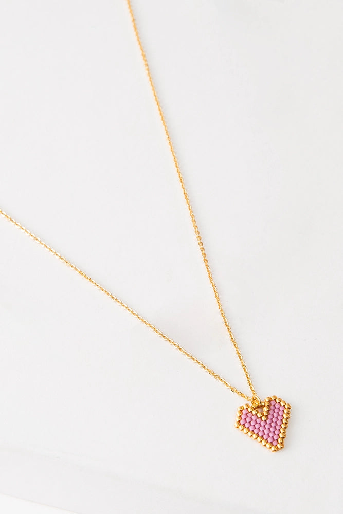 A small beaded heart hangs from a dainty gold chain. The heart pendant is flat and is composed of pink beads outlined with gold beads.