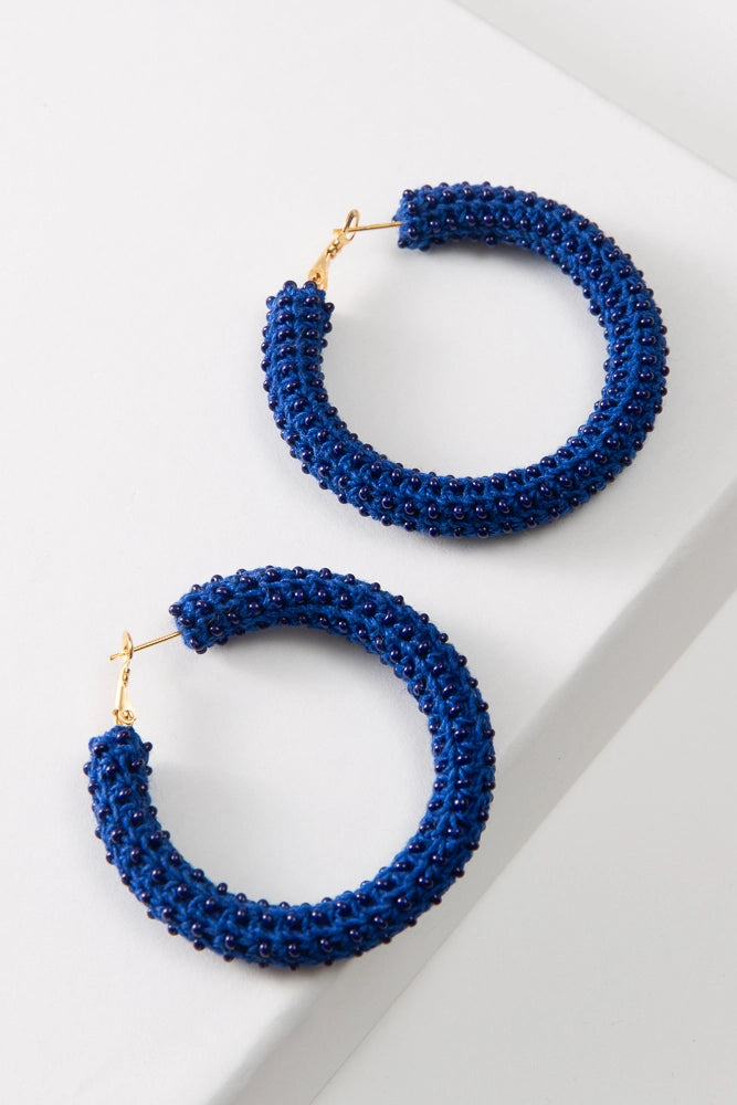 The Azul Crochet Hoops are large dark blue hoop earrings. Gold hoops are wrapped in blue crocheted thread studded all over with blue glass beads.