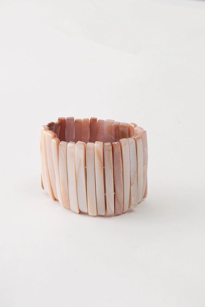 The Beachcomber Bracelet is composed of many tall strips of shell strung along elastic. The shell pieces vary in color, but each has peach and white tones.