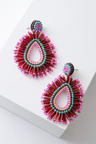 These are brightly colored teardrop-style earrings that are open at the center. The ear post is adorned with aqua, brown, and hot pink beads. Hanging down from the post is a large teardrop composed of layers of hot pink, yellow, brown, and aqua beads. Around the exterior of the teardrop, there is a beaded fringe composed of tubular red beads accented with hot pink seed beads.