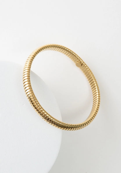 The Cobra Bracelet is a thin, simple gold bracelet. It has a banded texture that gives the look of a coil of shining gold wrapping around the wrist.