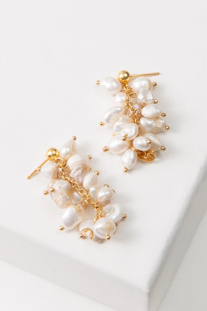 The Convertible Pearl Cluster Earrings are shown in their elongated form. The strand of pearls hangs down freely from the gold ear post for a chandelier-style earring.