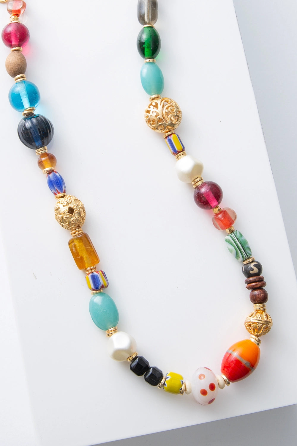 This is a single-strand necklace strung with a variety of beads in many shapes, sizes, materials, and colors. There are glass beads in a variety of styles, along with ceramic, bone, pearl, wood, and gold metallic beads. The beads are not arranged in a set pattern, creating a found objects feel.